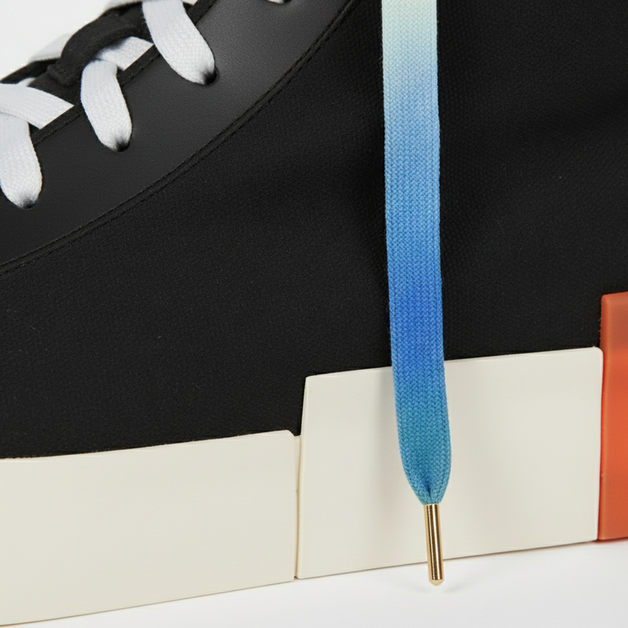 Black high-top sneakers with white - blue - green gradient shoelaces shown on a white background as a closeup 