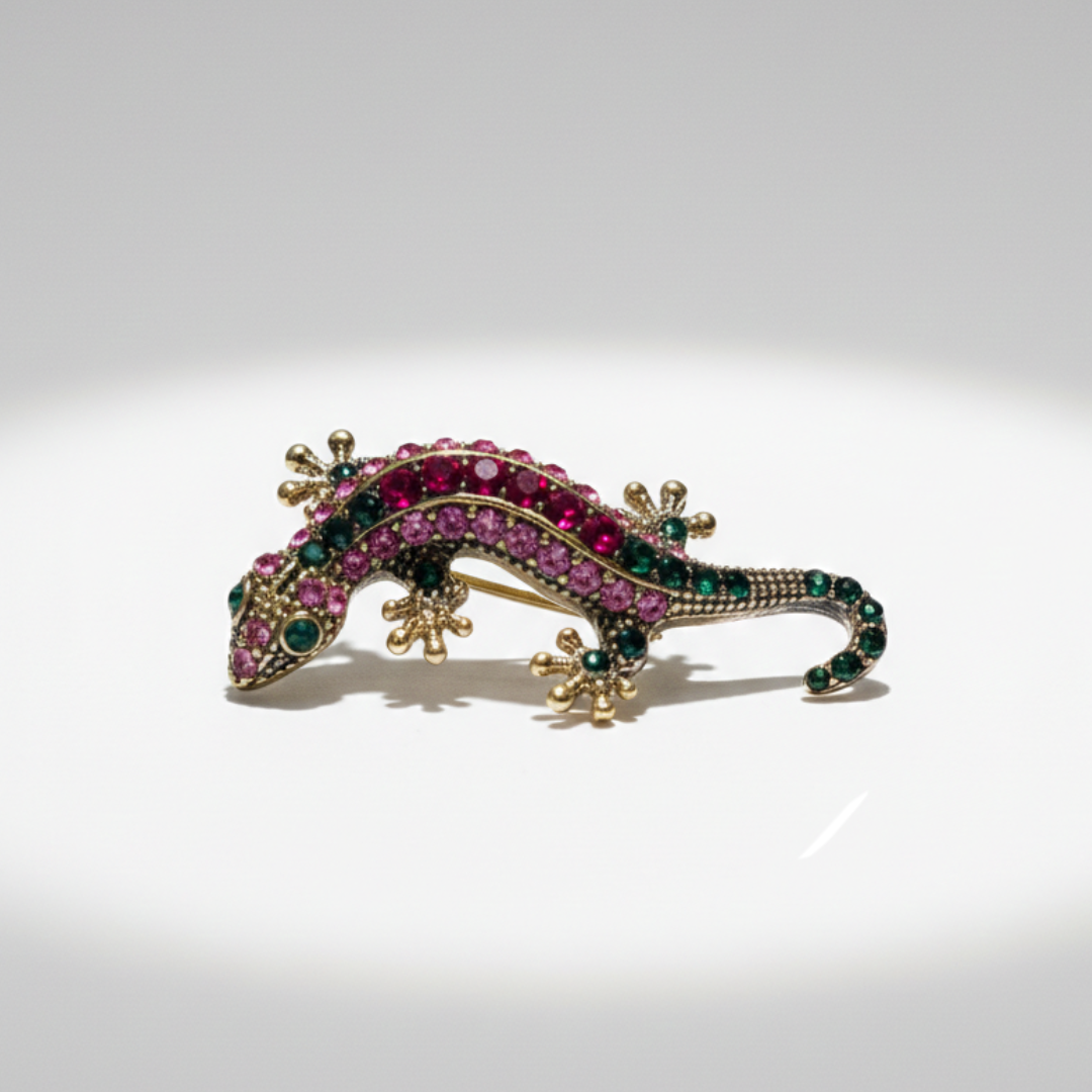Gold-tone gecko sneaker charm with pink and green crystal detailing on black background